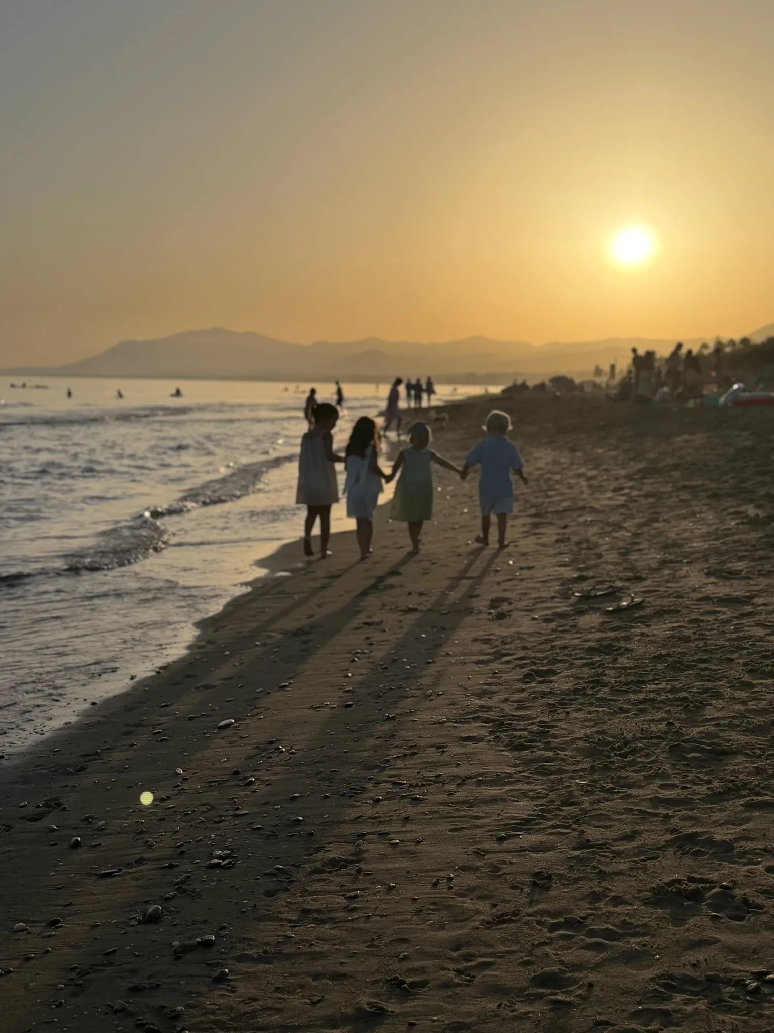 Children walking along the beach at sunset.