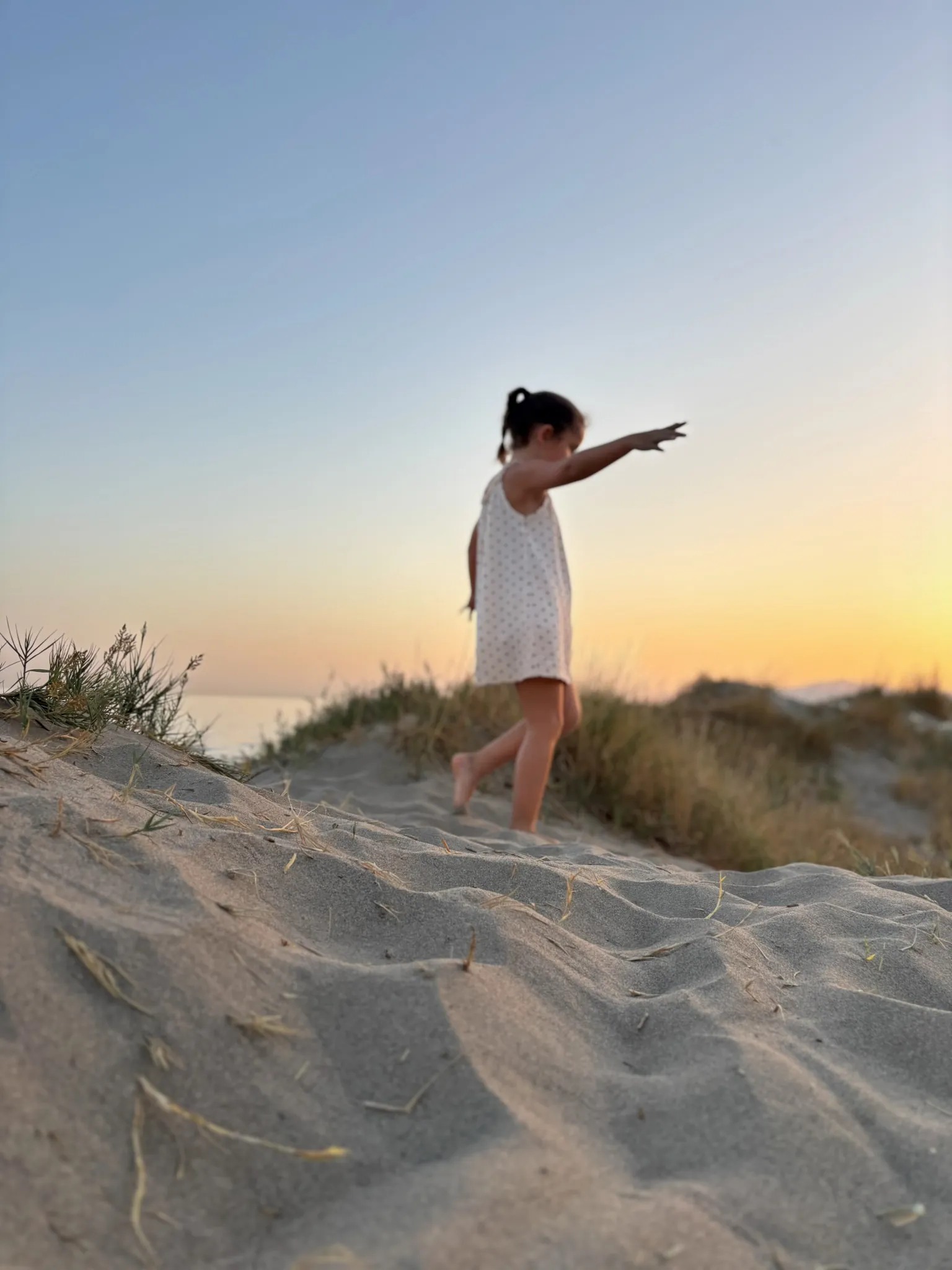 A child on a dune at sunset, arm stretched out.